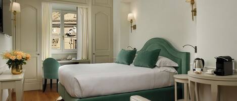 A neatly arranged hotel room with a bed, a desk, a chair, and a small table with a kettle and cup.