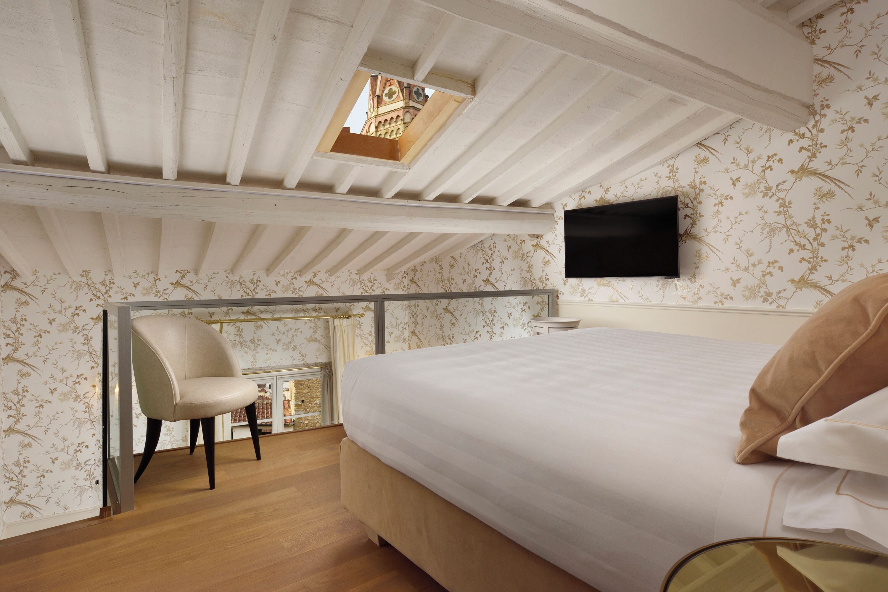 Un dormitorio con una cama grande, una silla, un televisor y una ventana pequeña con vista a un edificio.