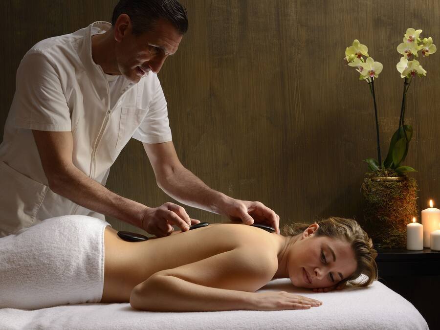 Une séance de massage dans un spa, avec un mur en bois et un vase rempli d’orchidées.