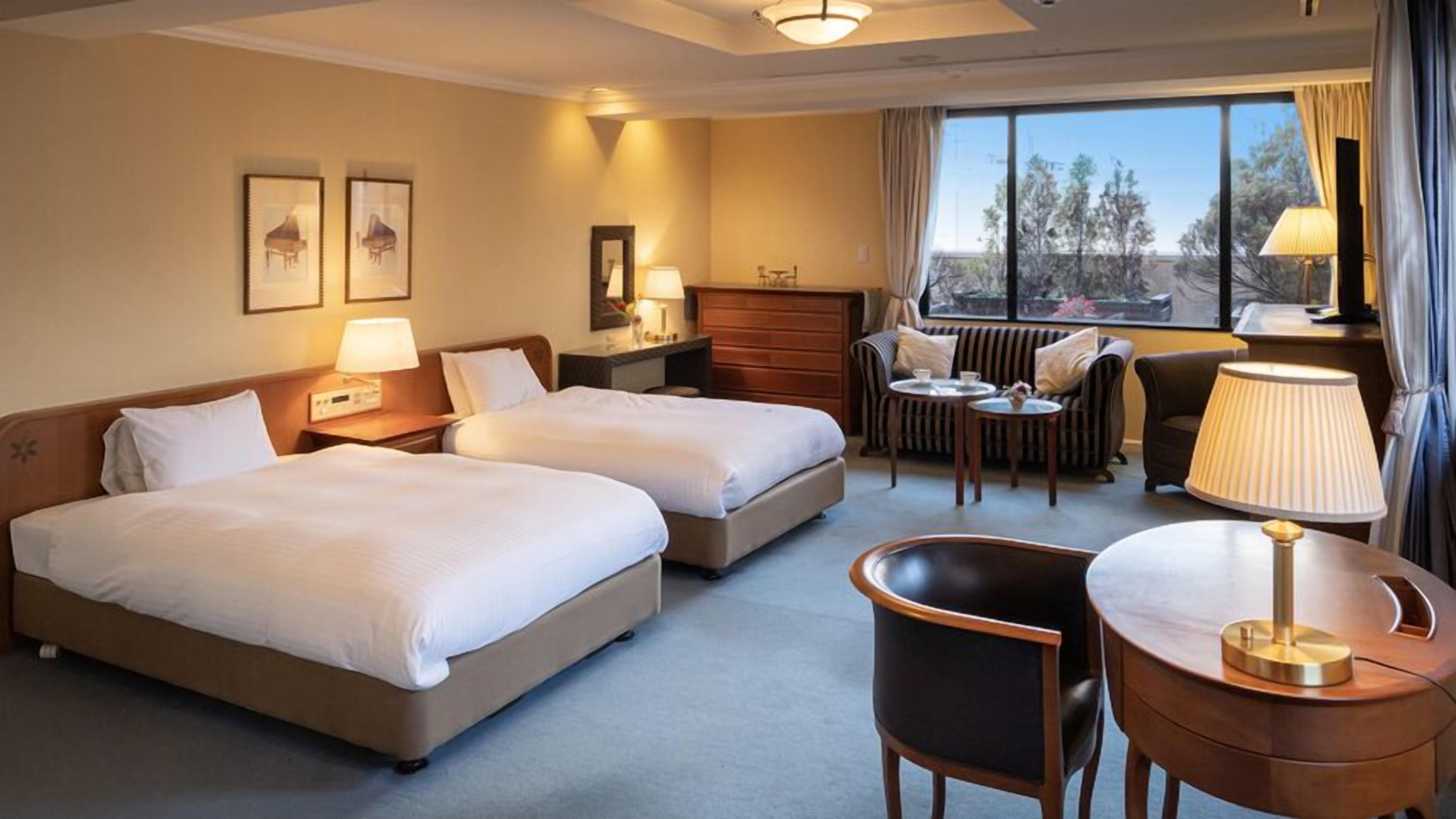A hotel room with two beds, a sofa, a chair, a small table, and a window with a view.