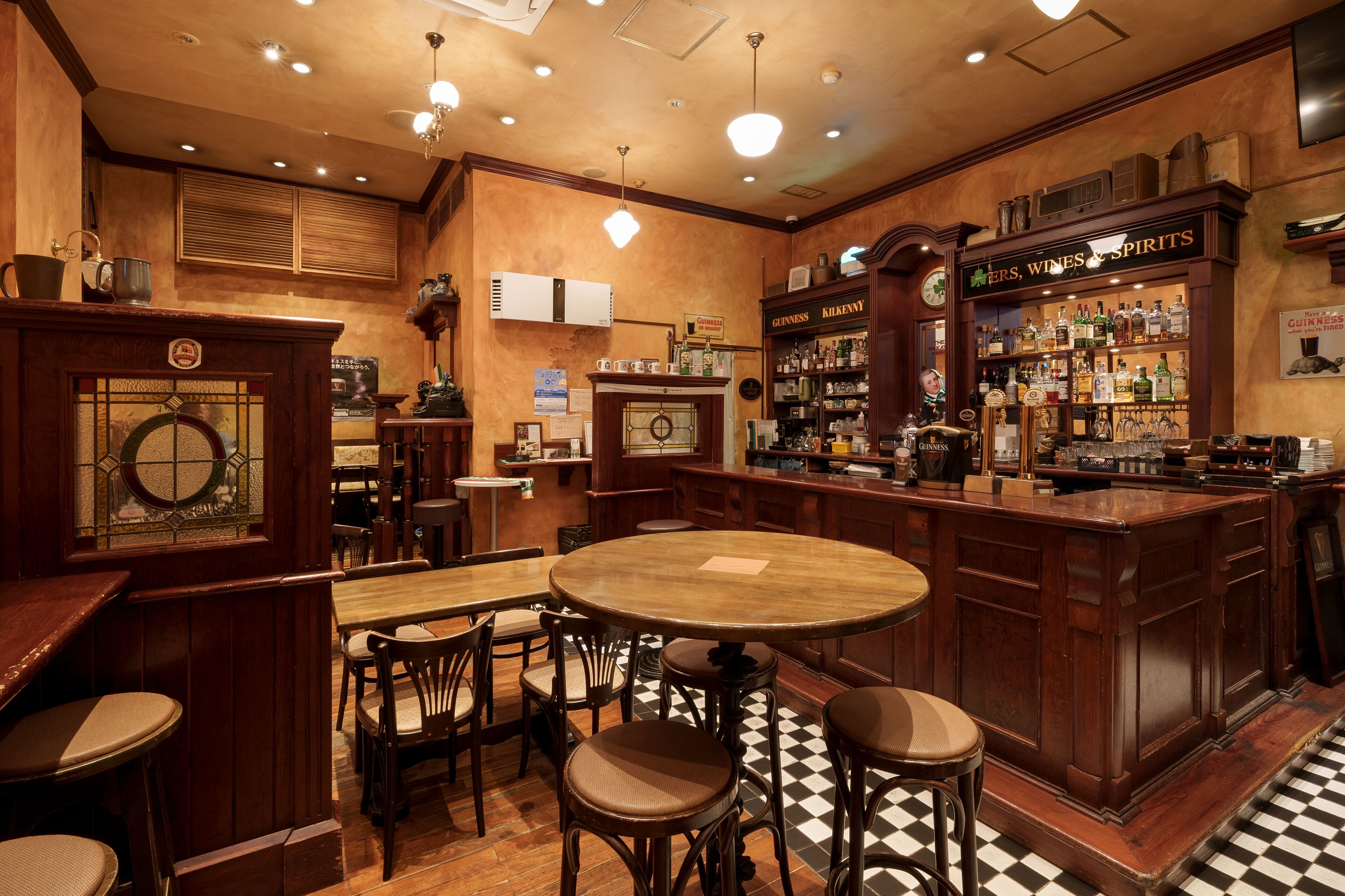 Un espace bar avec des meubles en bois, une table ronde et un comptoir avec des étagères remplies de bouteilles d’alcool.