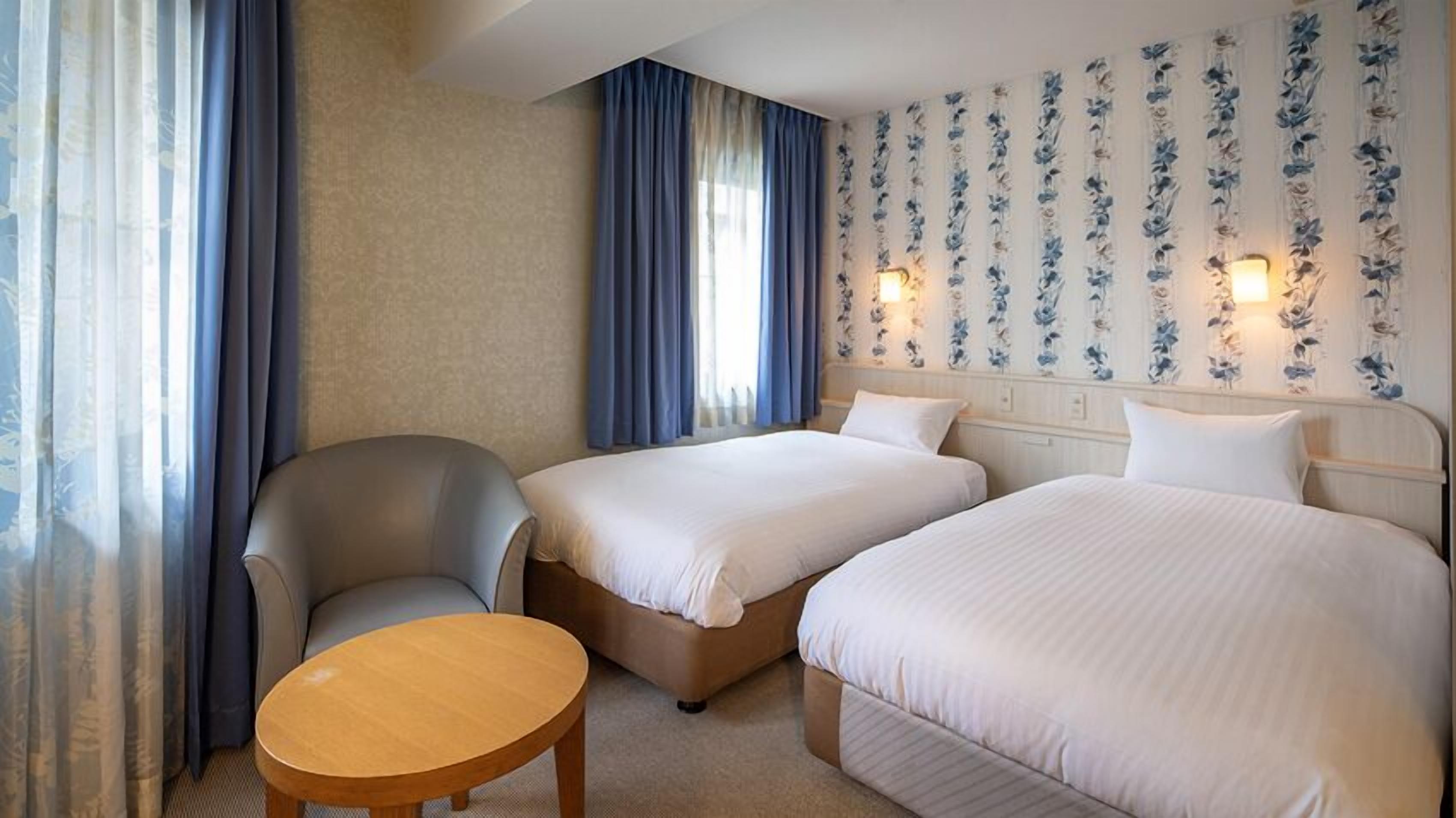 A hotel room with two beds, a chair, and a small table.