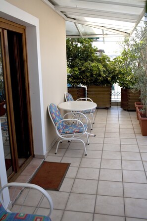 A covered patio area with a white table and chairs, potted plants, and a door leading to the interior. - Hotel Katerina (Athens)