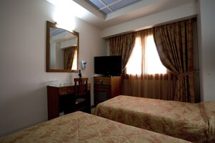 Una camera d'albergo con due letti, una scrivania con una sedia, una televisione e uno specchio.