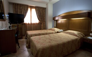Una camera d'albergo con due letti, televisione, minibar e finestra con tende.