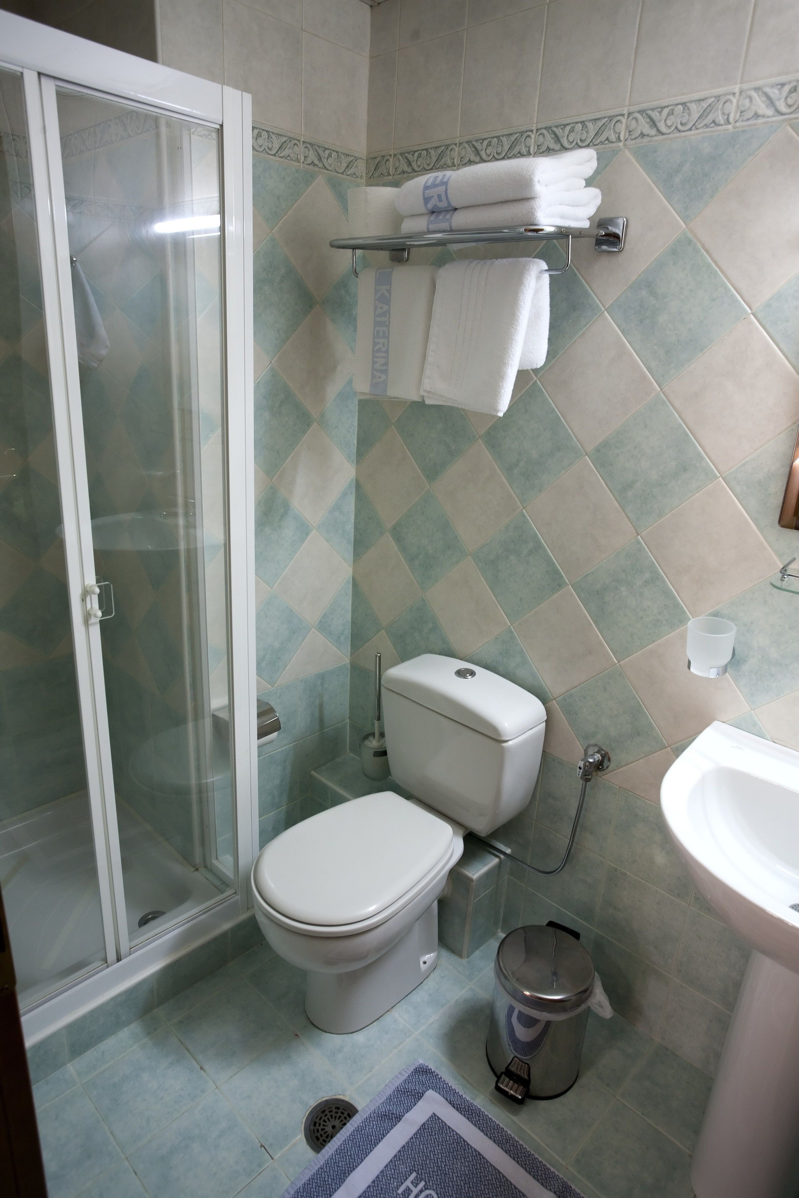Un bagno con doccia in vetro, un water, un bidet, un cestino e un portasciugamani con asciugamani piegati.