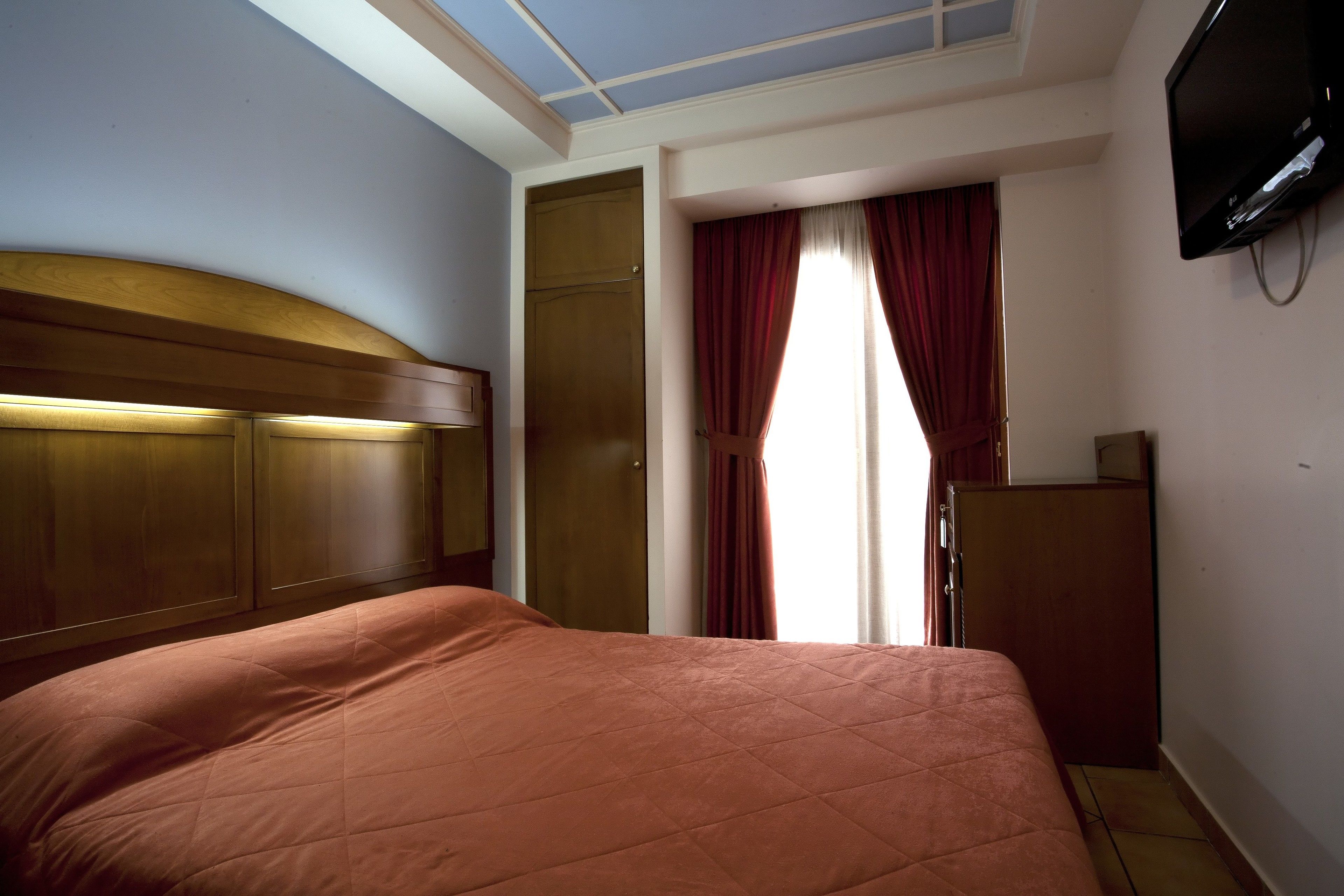 Een hotelkamer met een groot bed, een houten hoofdeinde, een televisie en een kledingkast.