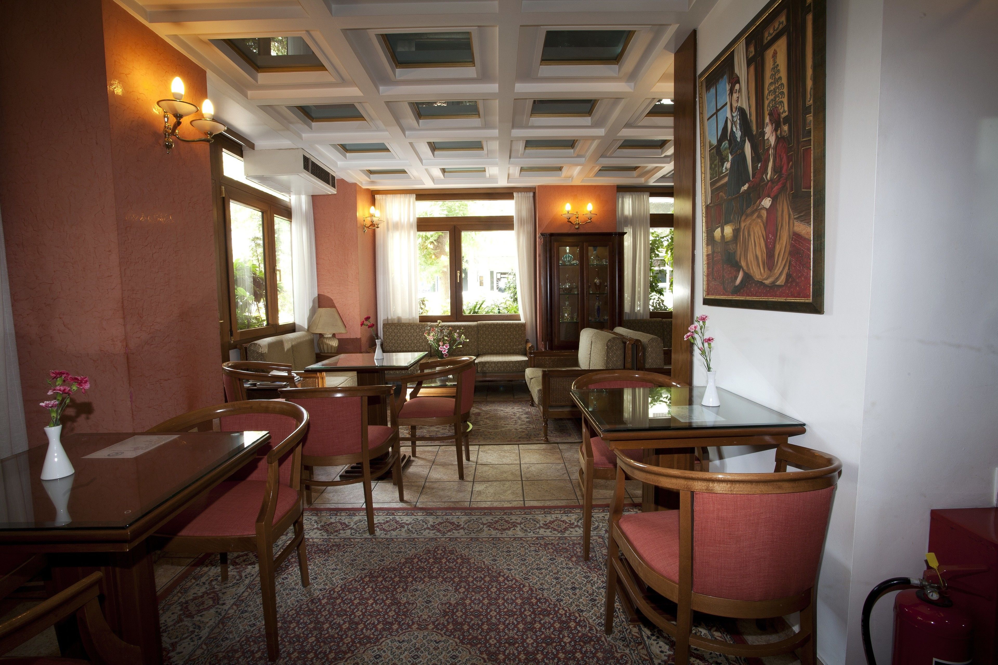 A dining area with wooden tables and chairs, a patterned rug, and a painting on the wall.