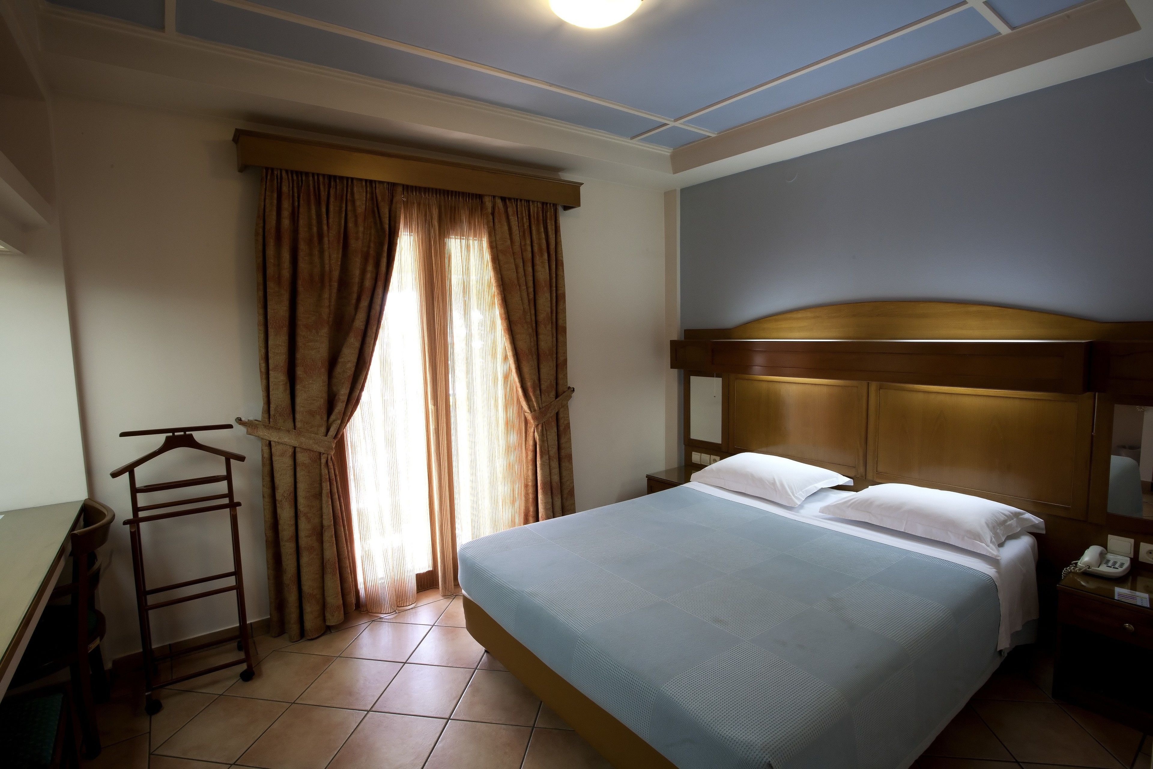 Una camera d'albergo con un letto, una scrivania, una sedia, un armadio e una finestra con tende.