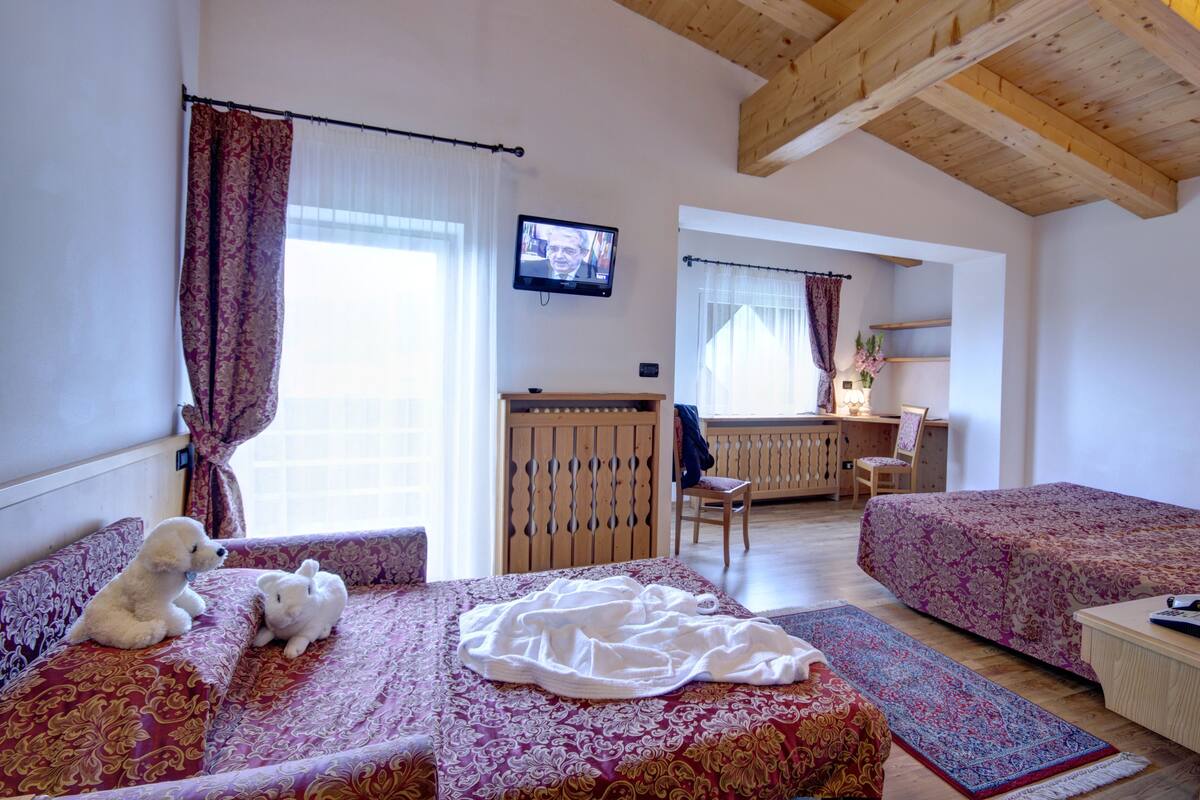 A bedroom with two beds, a desk, a TV, and a window with curtains.