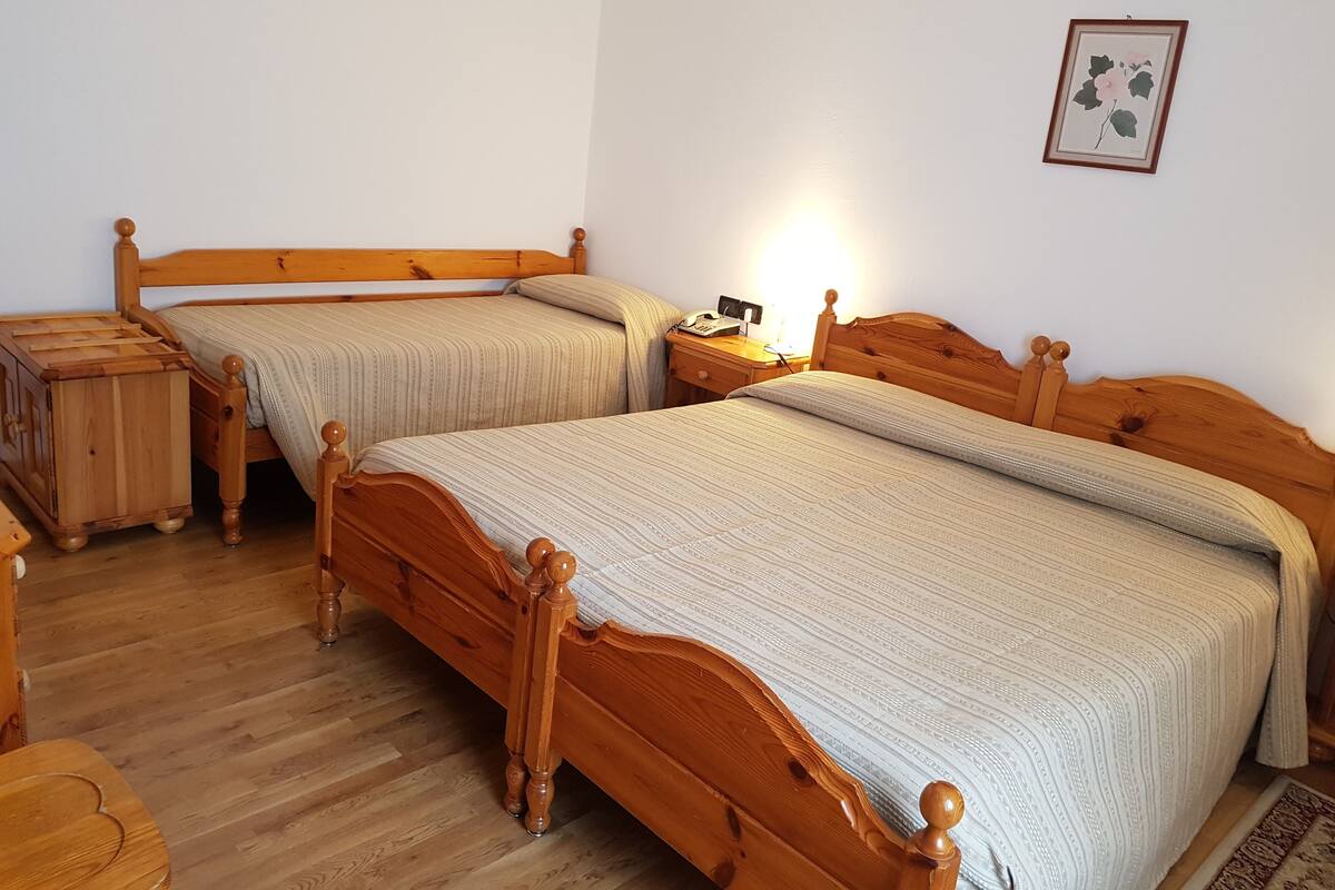 A bedroom with two wooden beds, a bedside table with a lamp, and a framed picture on the wall.