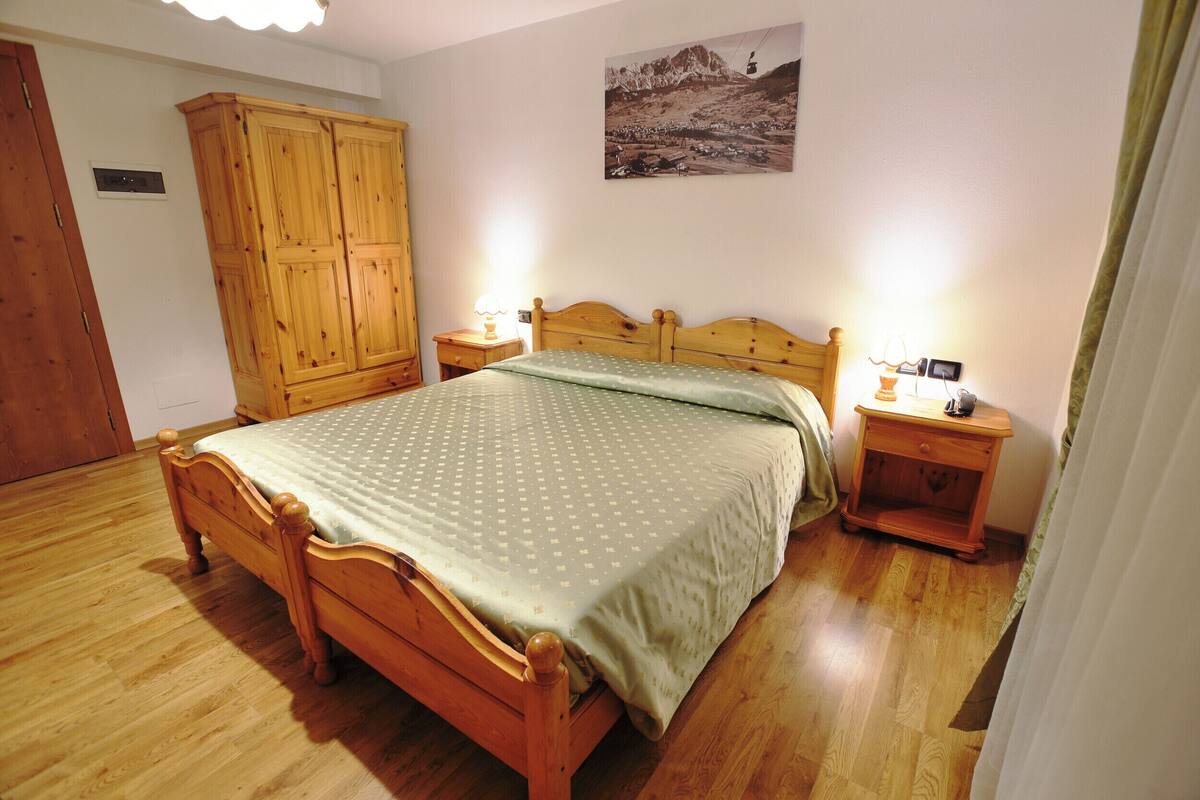 A bedroom with a wooden bed, a nightstand with a lamp, a wooden wardrobe, and a picture on the wall.