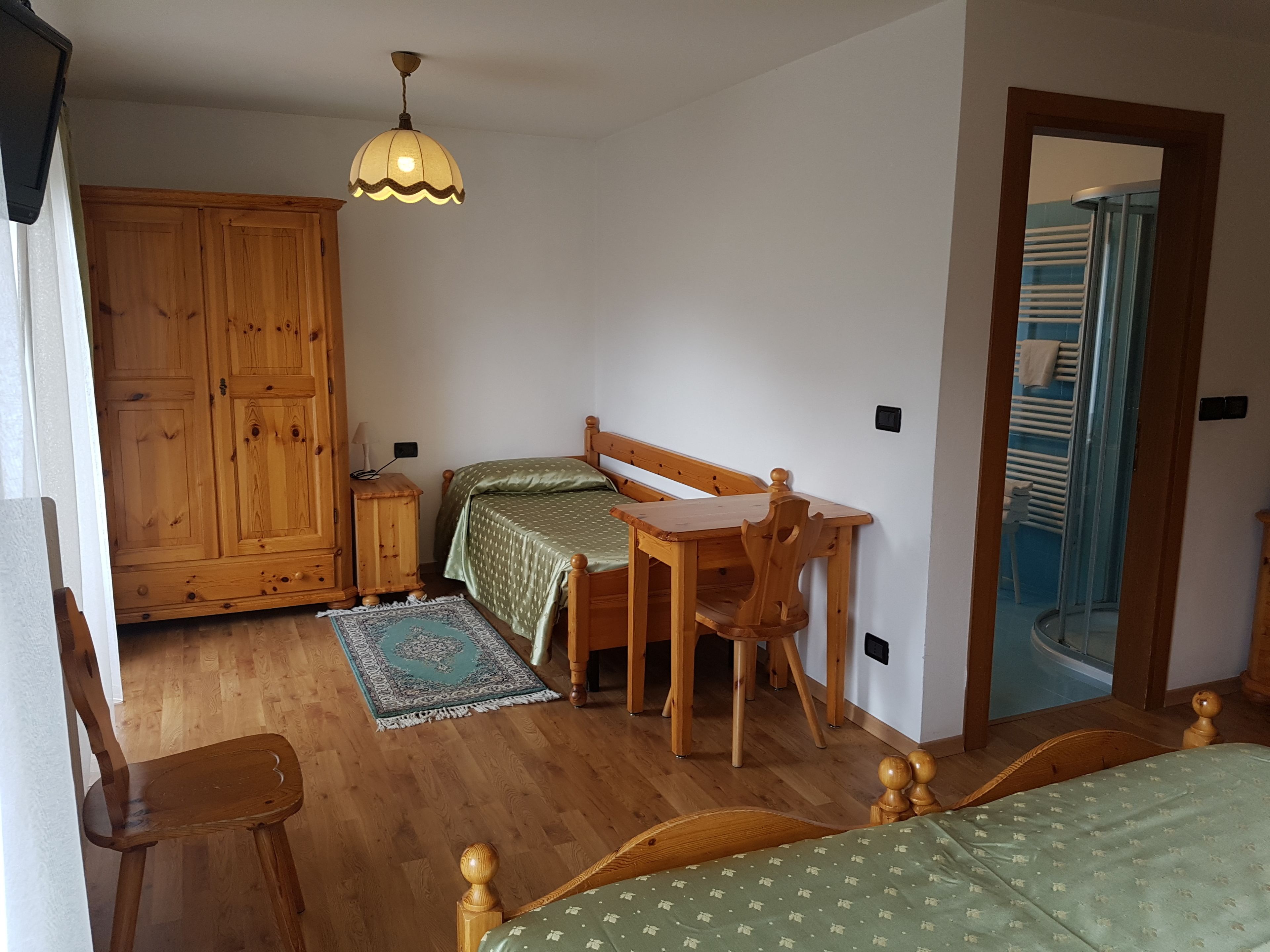 A bedroom with a wooden bed, a wooden desk, a nightstand, a wardrobe, and a bathroom visible through an open door.