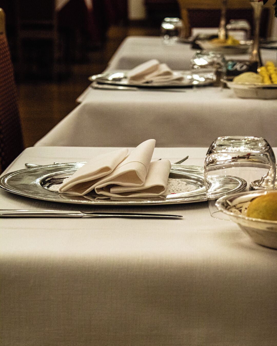 A table set with plates, folded napkins, cutlery, and a glass.