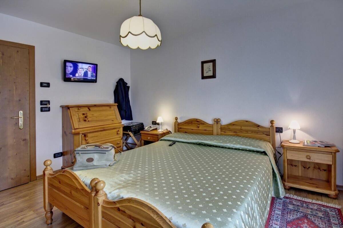 A bedroom with a wooden bed, a television on the wall, a lamp on the nightstand, and a door.