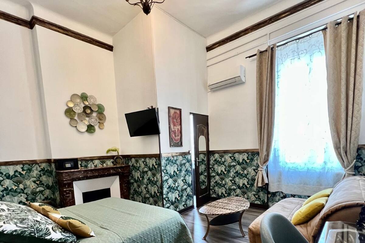 Quarto com duas camas, uma mesinha, uma cadeira, uma TV e uma janela com cortinas.