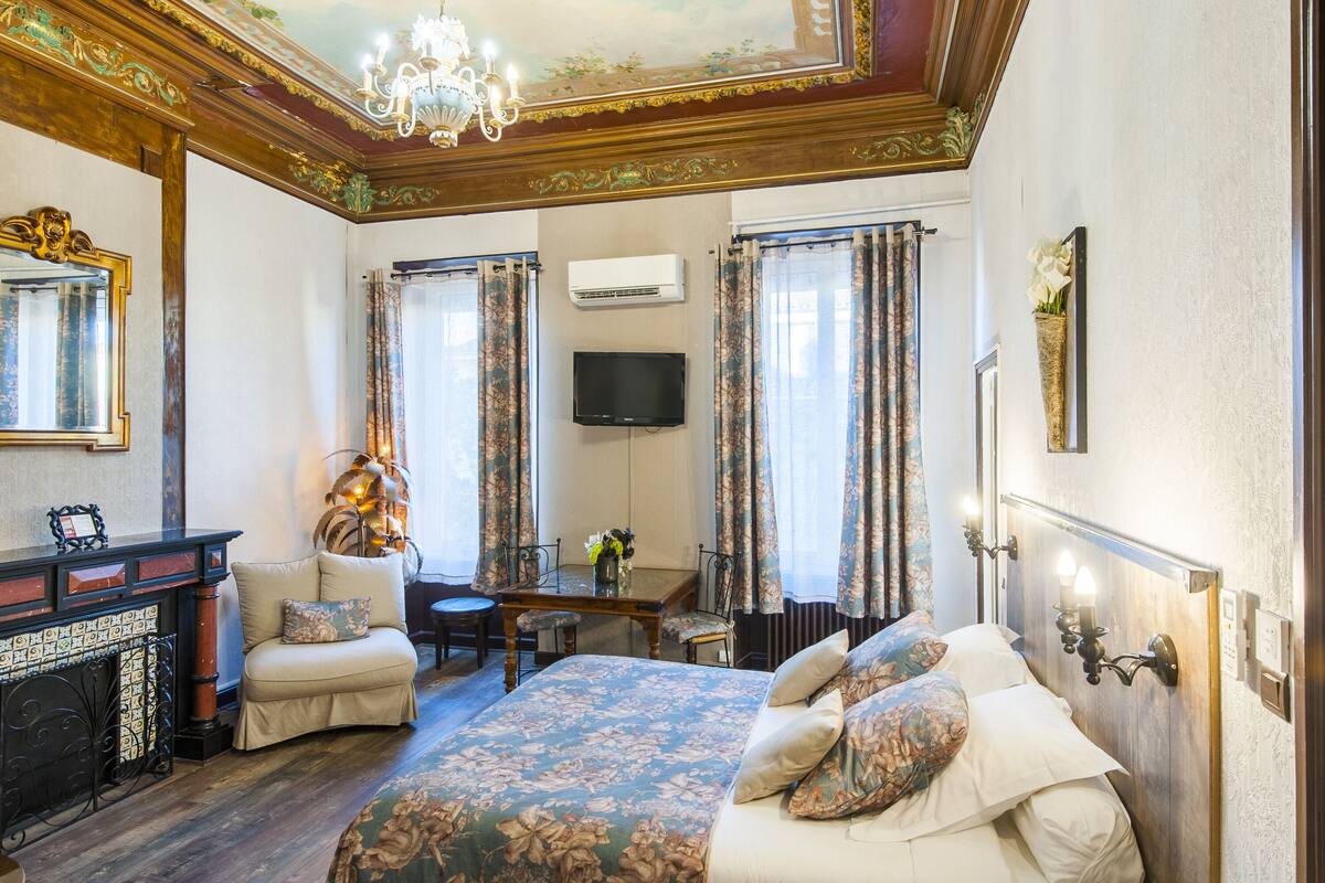Quarto de hotel com uma cama grande, uma escrivaninha com cadeira, lareira e televisão.