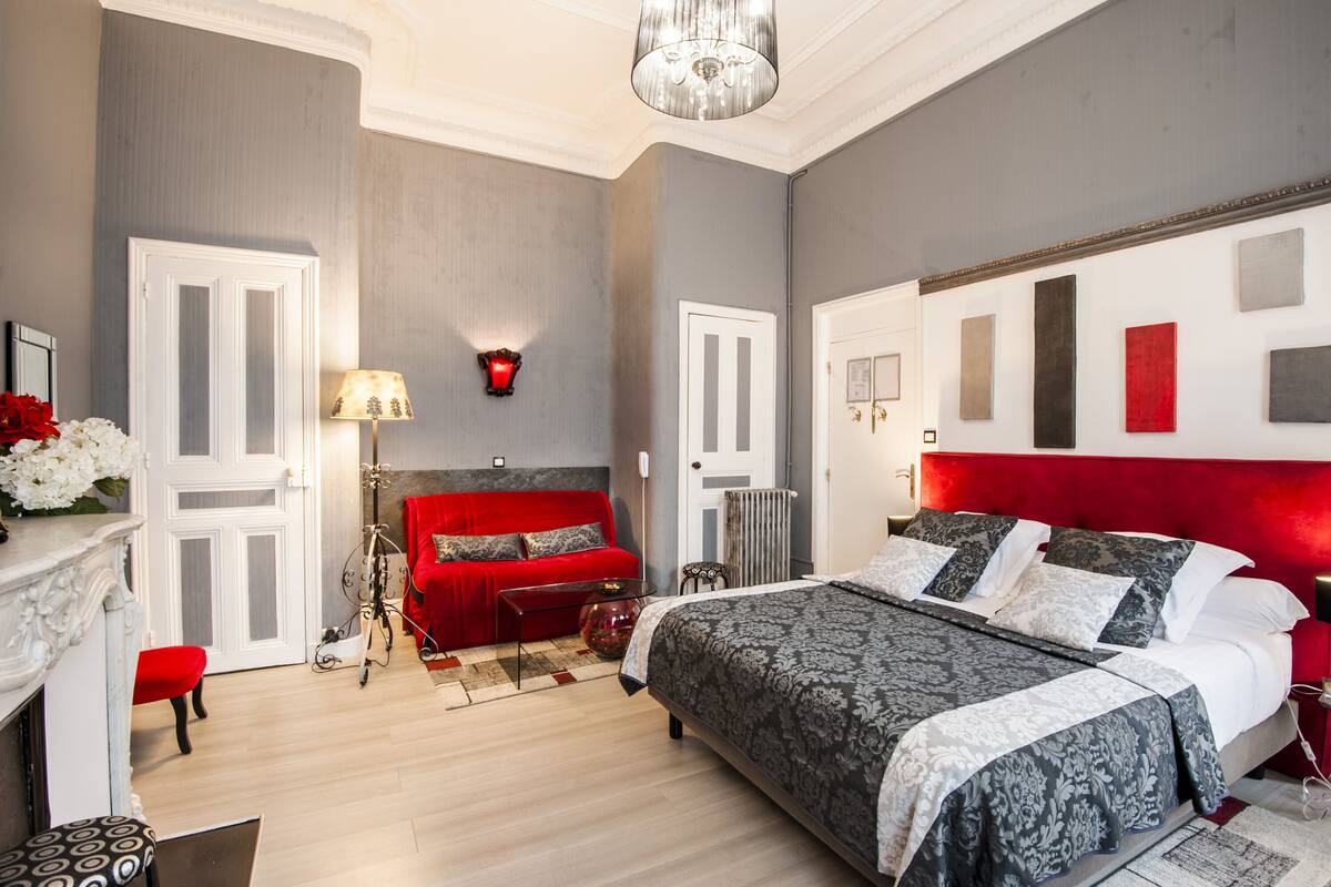 Quarto moderno com uma cama grande, um sofá vermelho, uma escrivaninha com abajur e um lustre.