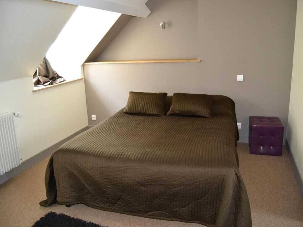 A bedroom with a sloped ceiling, a bed with a brown cover, a window, and a radiator.