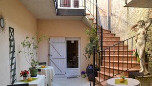 A courtyard with a staircase, tables, chairs, and potted plants. - Hotel de La Poste (Clamecy)