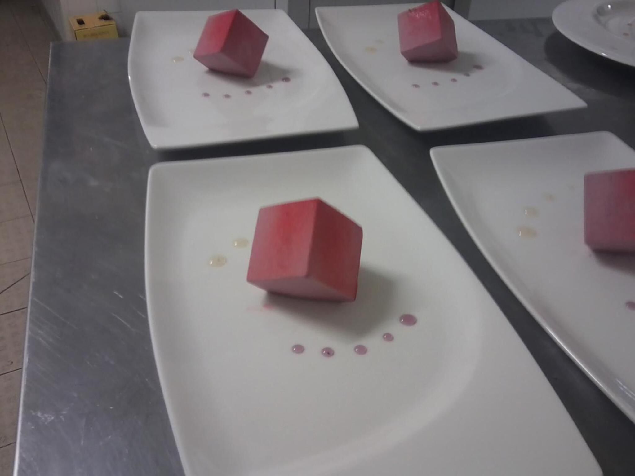 Ein Tisch mit mehreren quadratischen Tellern, auf jedem ein rotes Würfel-Dekor und einige kleine rosa Punkte.