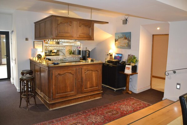 A bar area with wooden cabinets, a bar counter, stools, and a laptop on a small table.