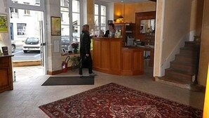 A hotel lobby with a reception desk, a staircase, and a large patterned rug. - Hotel de La Poste (Clamecy)