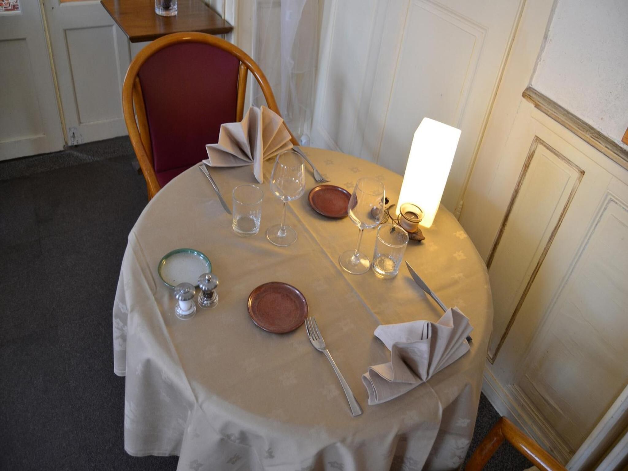 Une table à manger dressée avec des assiettes, des verres et des couverts, une bougie et un présentoir à menus.