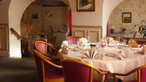 A dining area with round tables, red upholstered chairs, and a classic European architectural style with arched doorways and framed artwork on the walls. - Hotel de La Poste (Clamecy)