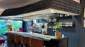 Zona de bar con mostrador negro, taburetes de madera y una lámpara colgante.