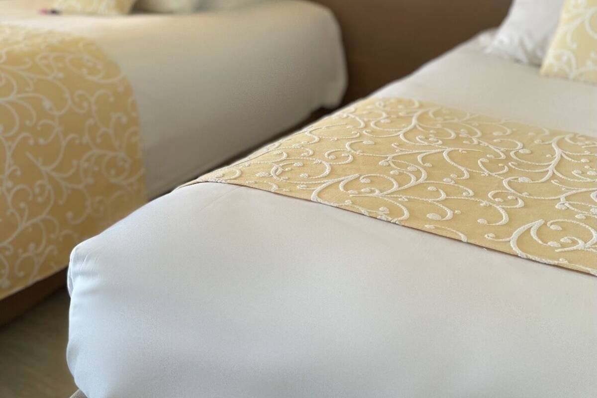 Quarto de hotel com duas camas, cada uma com colcha e almofadas estampadas.