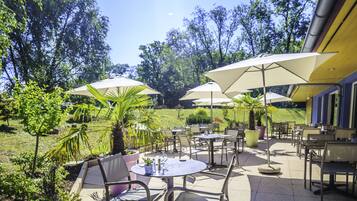 Een terras buiten met ronde tafels en stoelen, omringd door parasols en potplanten.