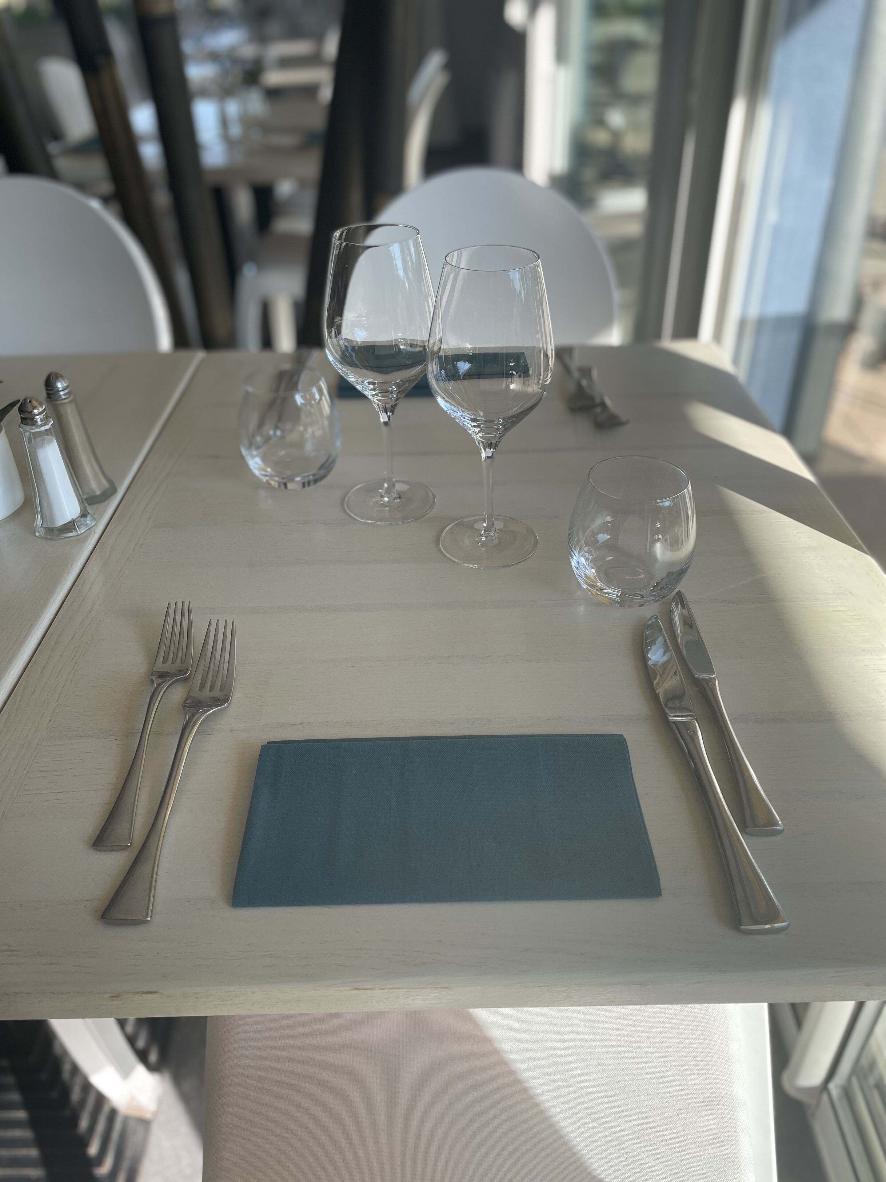 Una mesa de comedor dispuesta con copas de vino, cubiertos y saleros y pimenteros.