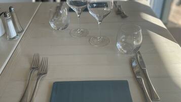 Una mesa de comedor dispuesta con copas de vino, cubiertos y saleros y pimenteros.