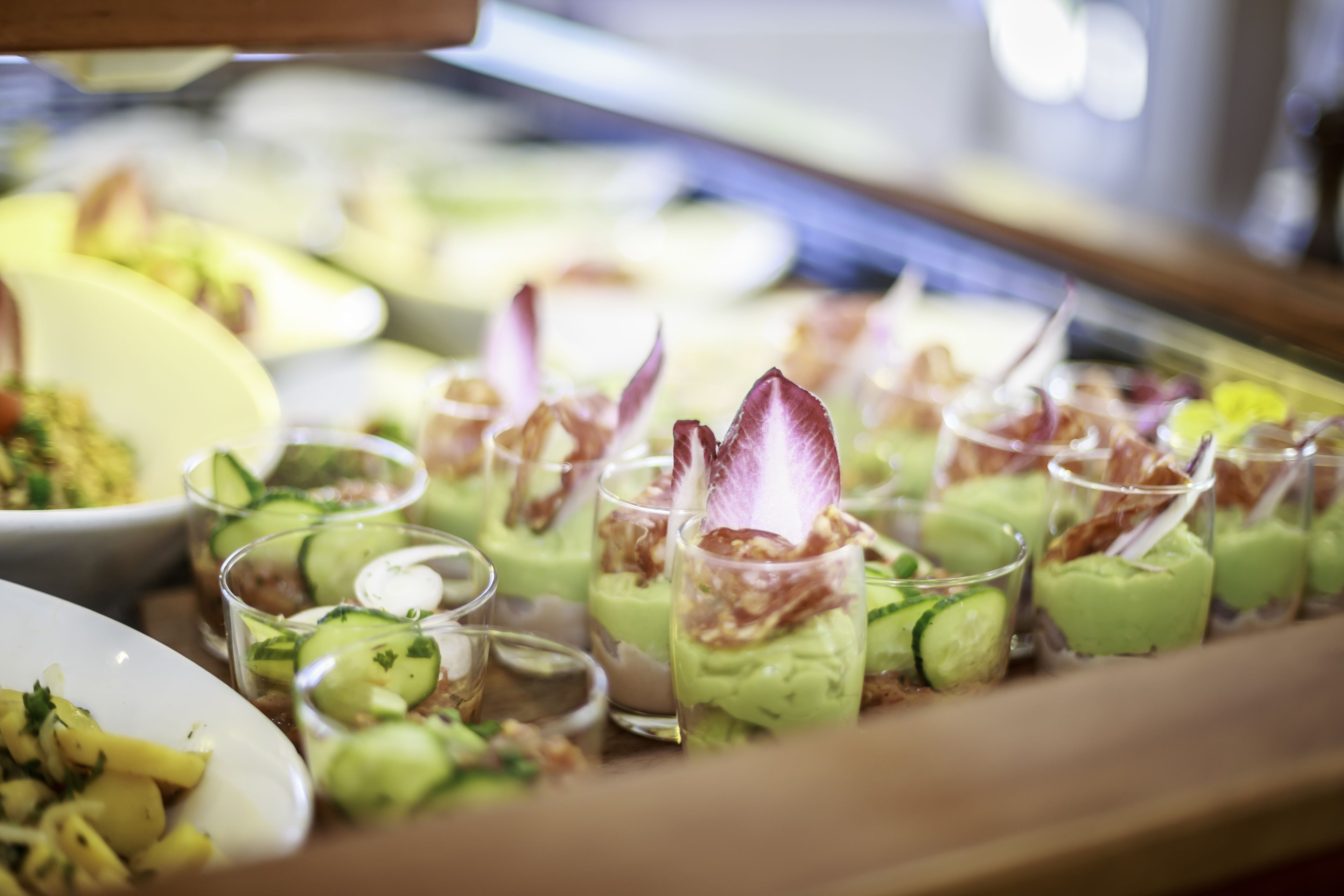 A buffet with various dishes, including a green dessert and a salad with cucumber slices.