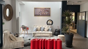 Una sala de estar moderna con un sofá, un reposapiés rojo, una planta en maceta y un espejo grande.