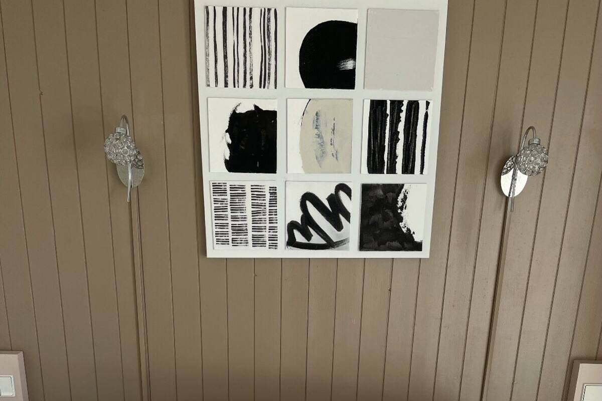 Cama bem arrumada com duas almofadas decorativas, uma obra de arte abstrata emoldurada acima dela e duas luminárias fixadas na parede, uma de cada lado.