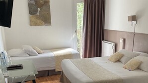 Una habitación de hotel con dos camas individuales, un escritorio con silla, un televisor montado en la pared y una ventana con cortinas.