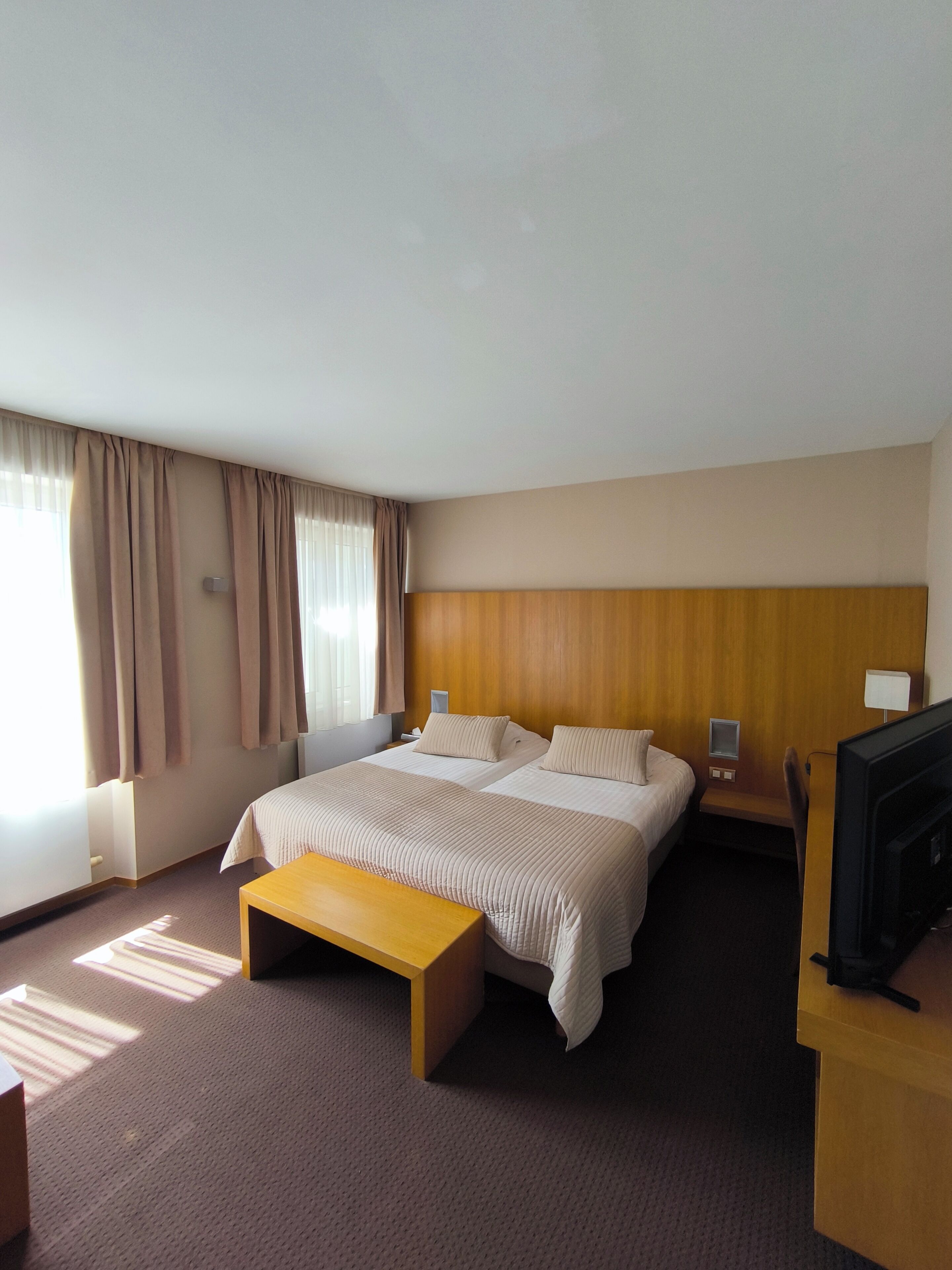 Una habitación de hotel con una cama grande, cabecera de madera, televisor y escritorio.