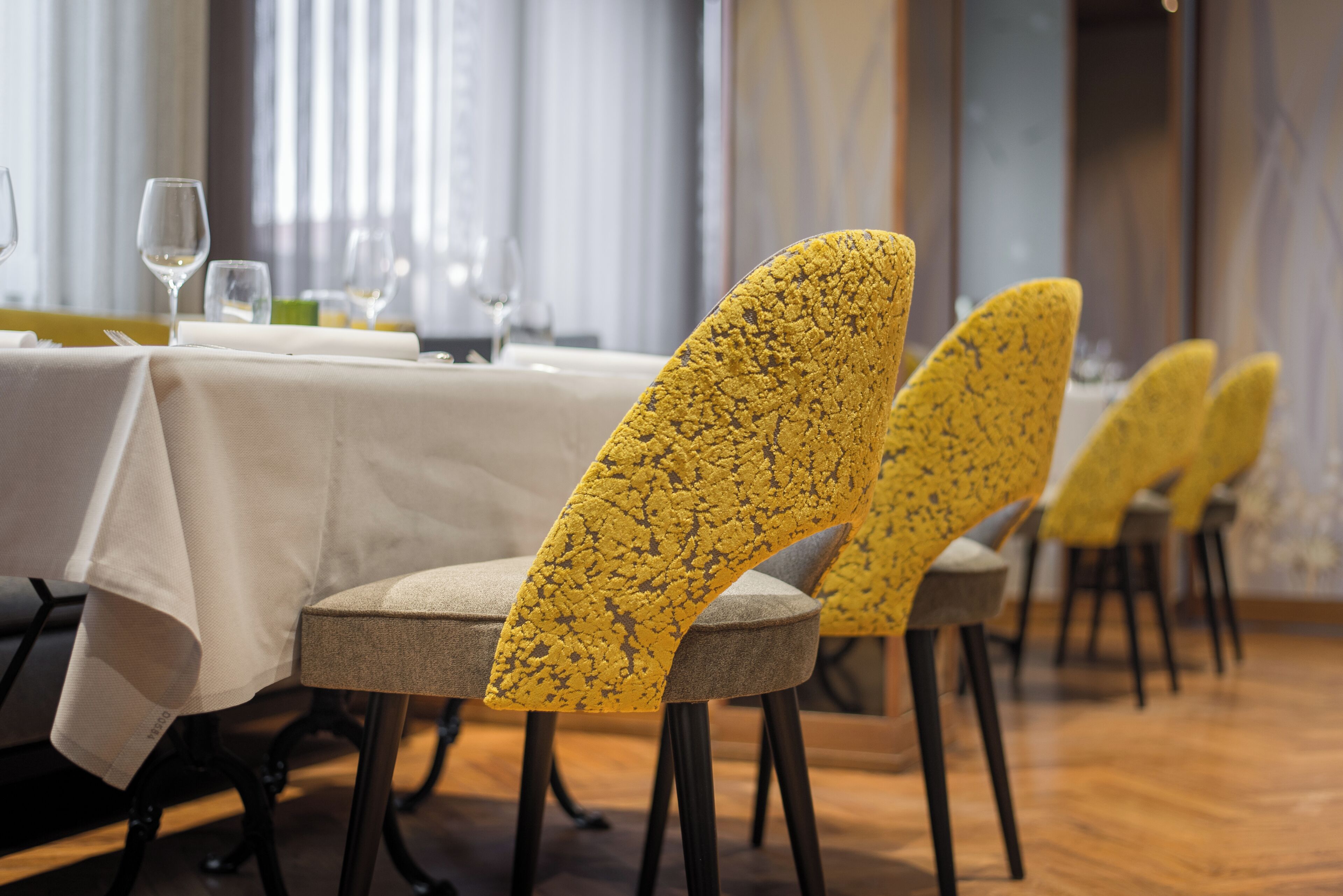 A dining area with tables set for service, chairs with a textured yellow upholstery, and a wooden floor.