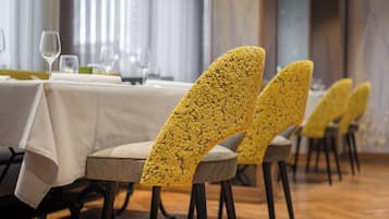 A dining area with tables set for service, chairs with a textured yellow upholstery, and a wooden floor.