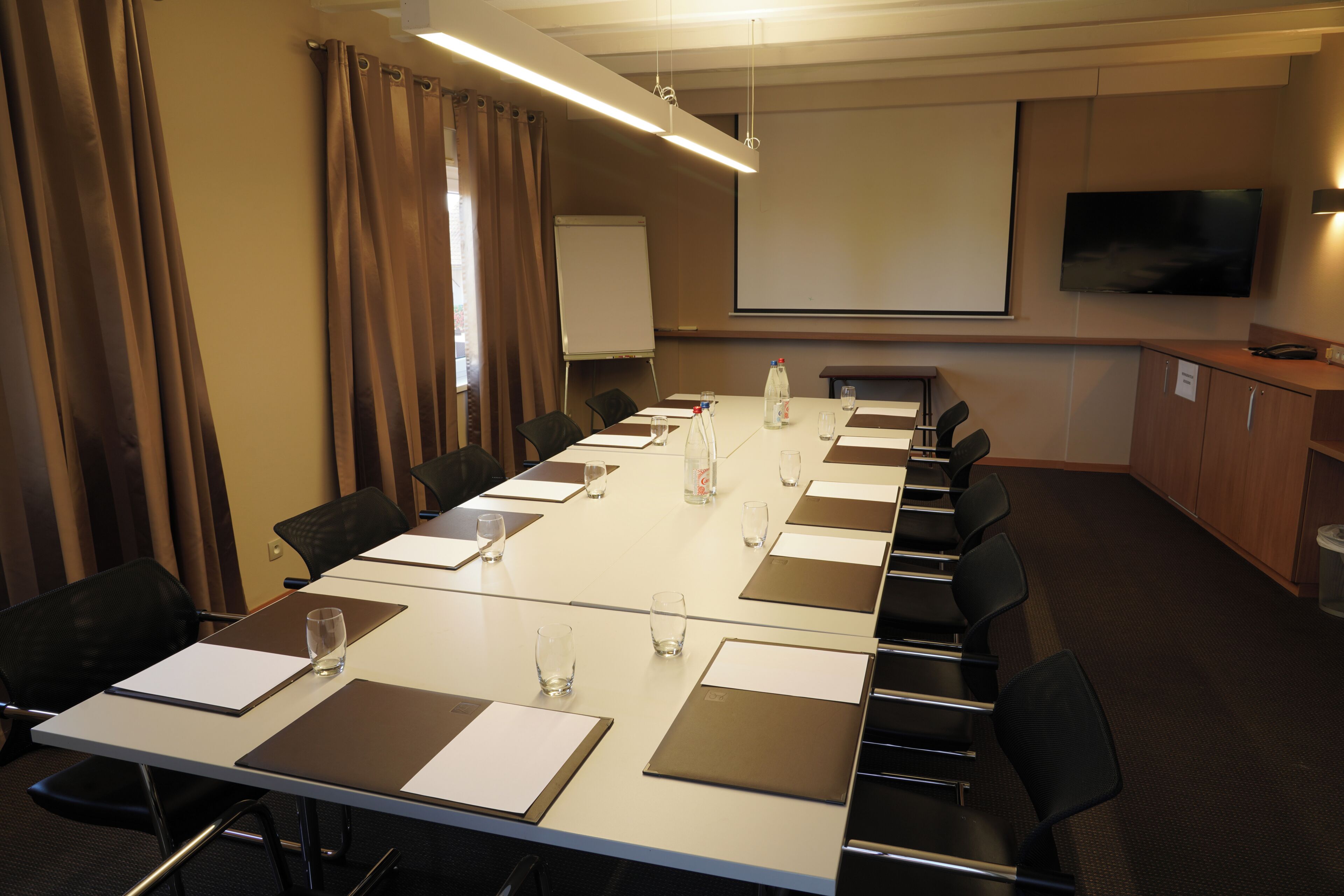 Un salón de conferencias con una larga mesa, sillas, una pantalla de proyector y una televisión.