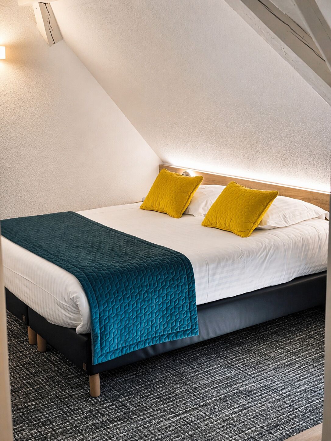 Une chambre à coucher avec un lit, deux oreillers, une couverture de couleur turquoise et un tapis à motifs.