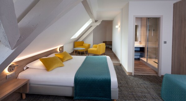 Habitación de hotel moderna con una cama grande, un escritorio, una silla y una mesita. Se ve un baño a través de una puerta de cristal.