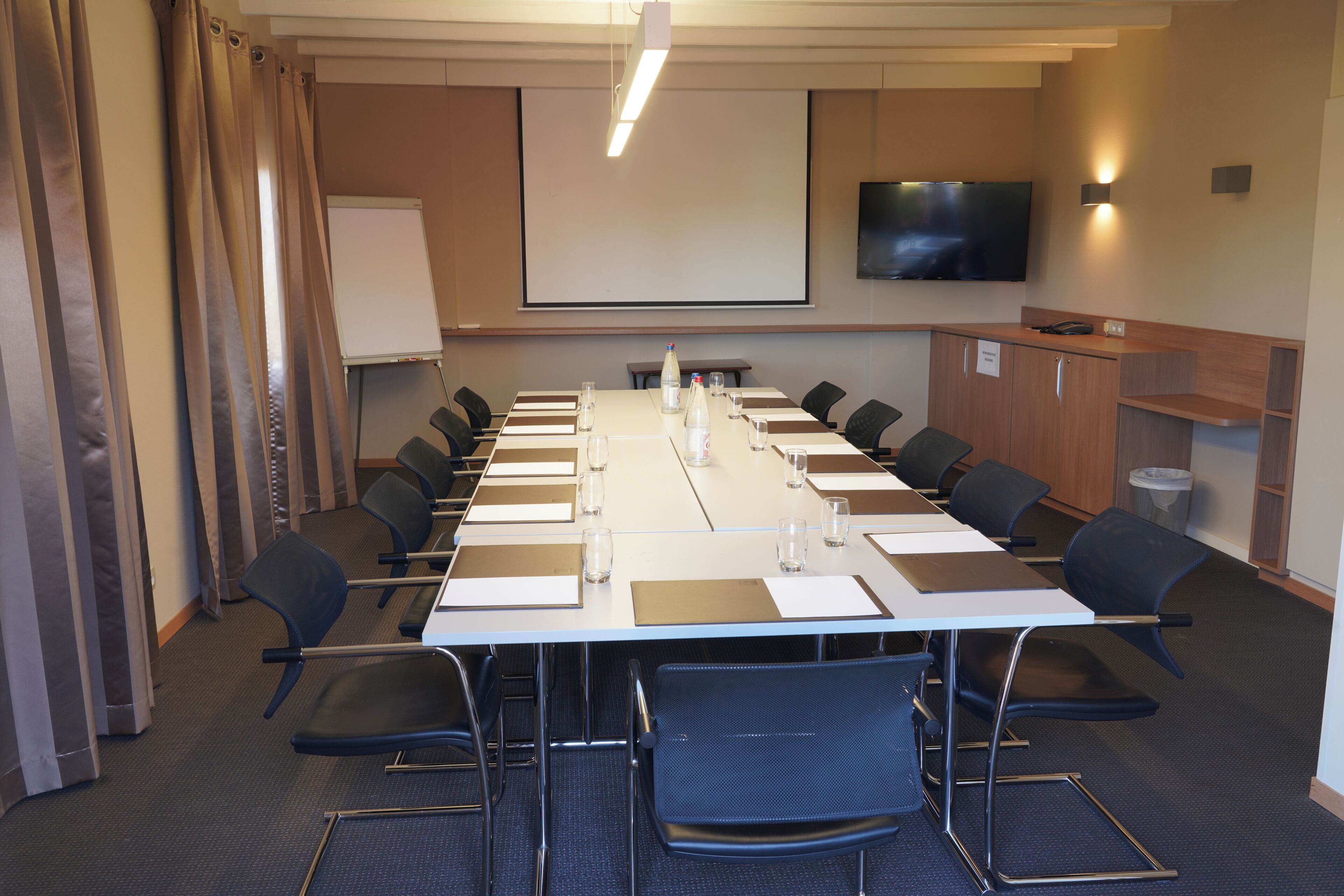 Une salle de conférence équipée d’une longue table, de chaises, d’un tableau blanc, d’un écran et d’un téléviseur.