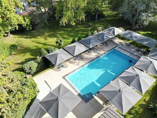 A swimming pool with surrounding lounge chairs and umbrellas, surrounded by a well-maintained lawn and trees. - Hôtel Restaurant Groff Aux Deux Clefs (Biesheim)