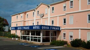 Un hotel llamado 'Quick Palace' con fachada rosa, múltiples ventanas y un letrero que indica acceso para sillas de ruedas.