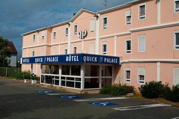 Un hotel llamado 'Quick Palace' con fachada rosa, múltiples ventanas y un letrero que indica acceso para sillas de ruedas.