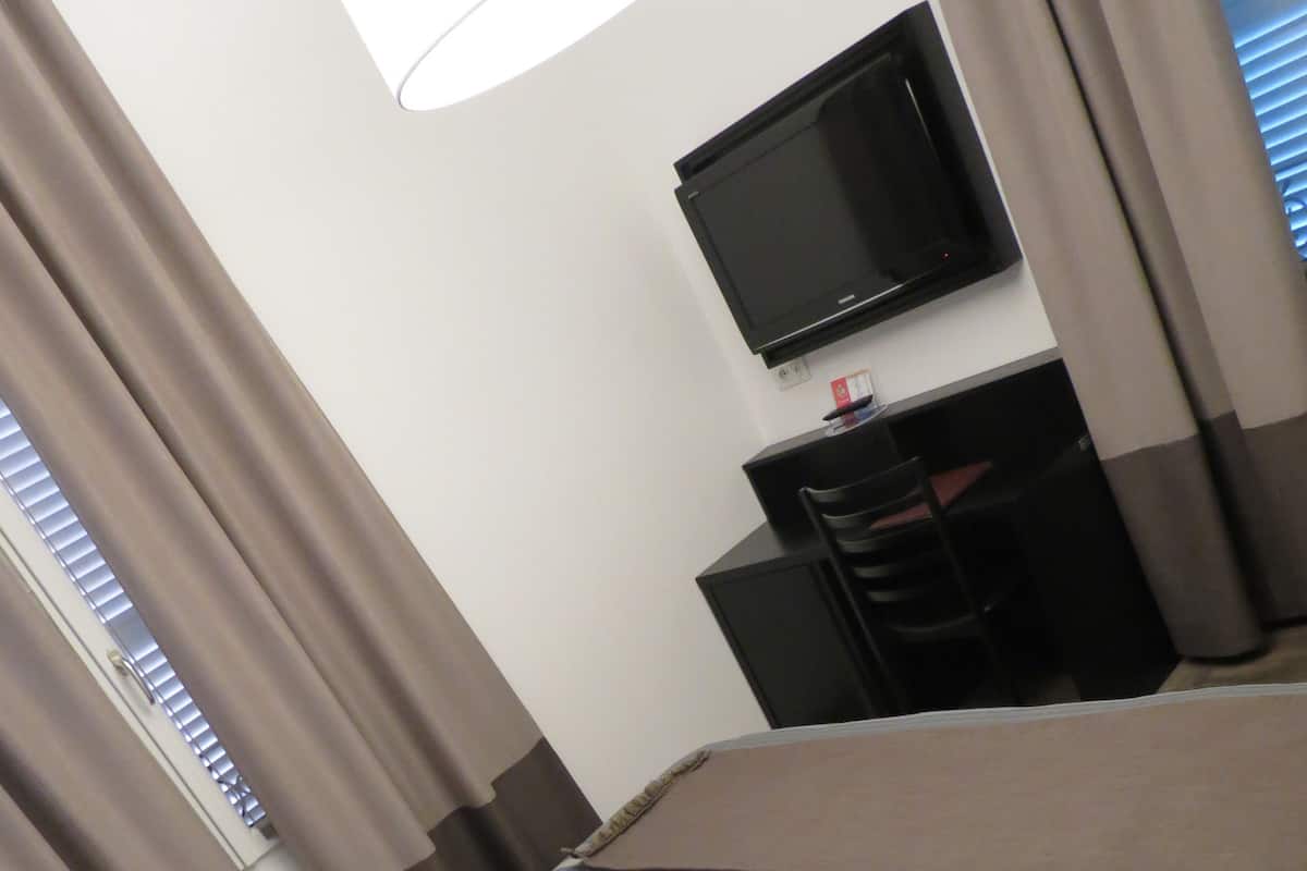 A hotel room with a bed, a television on a stand, and a desk with a chair.