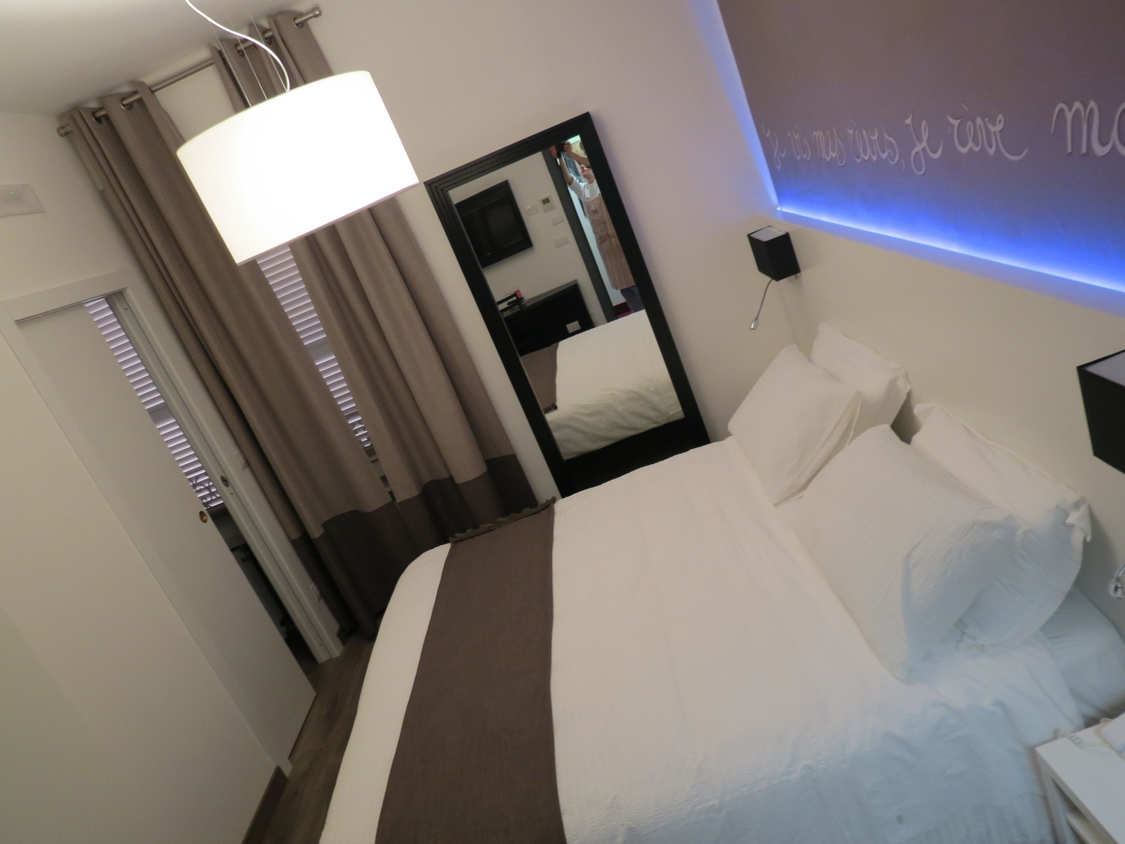 Una habitación de hotel con una cama, una lámpara de noche, un espejo y una lámpara de pared.